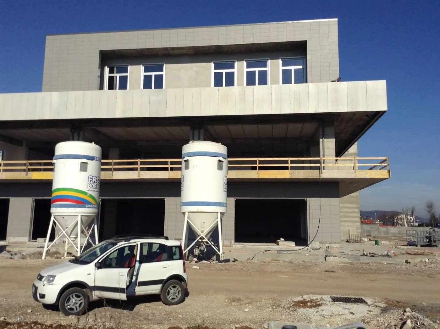 Fiano Romano: fronte dell’edificio in costruzione con solai a sbalzo, silos e un’auto di cantiere in primo piano.