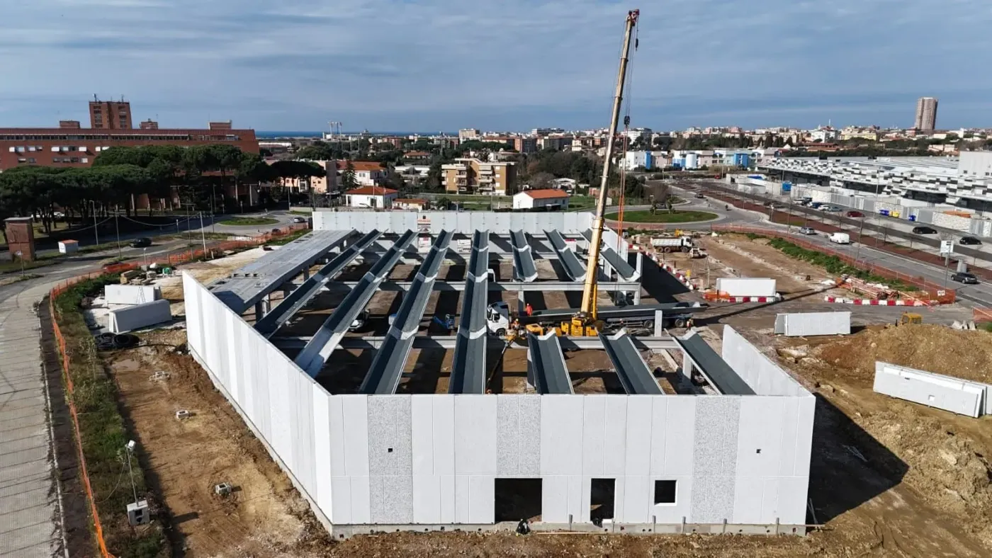 Fabbricato prefabbricato in montaggio: pannelli perimetrali, travi di copertura e autogru, ripresa da drone.